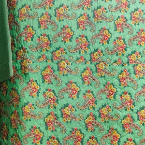 Könnte beinhalten: Gesteppter Stoff mit sich wiederholendem Paisley-Muster in Rot, Gelb und Braun auf grünem Hintergrund. Die Steppdecke hat ein Rautenmuster und einen einfarbigen grünen Rand.