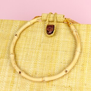 Puede incluir: Un bolso de mano de paja tejida con un asa de bamb&uacute; natural. El asa est&aacute; asegurada con una pieza de cuero marr&oacute;n.