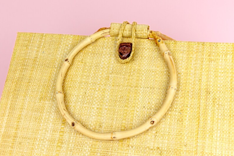 Puede incluir: Un bolso de mano de paja tejida con un asa de bamb&uacute; natural. El asa est&aacute; asegurada con una pieza de cuero marr&oacute;n.