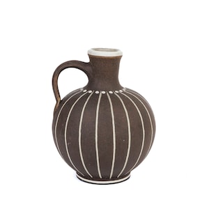 May include: A brown ceramic pitcher with a handle and a rounded body. The pitcher is decorated with vertical white stripes and a white rim. The overall design is simple and elegant, suitable for serving beverages or as a decorative item.