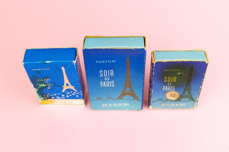 Puede incluir: Tres cajas de perfume azules y doradas con el texto "Parfum Soir de Paris Bourjois" y una imagen de la Torre Eiffel.