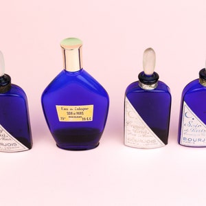 May include: Four blue glass bottles of perfume with silver and gold accents. The bottles are labeled "Evening in Paris" and "Soir de Paris" by Bourjois Paris.