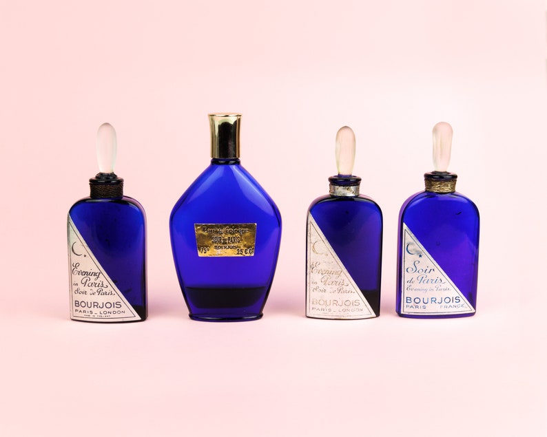 May include: Four blue glass bottles of perfume with gold accents and labels that read "Evening in Paris" and "Soir de Paris".