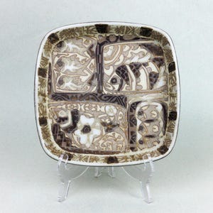 May include: Square ceramic dish with a decorative pattern in shades of brown, beige, and white. The dish is divided into four sections, each with a unique design featuring floral and abstract motifs. The rim has a dark brown border.