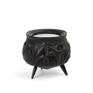 Peut inclure: Un chaudron noir à trois pieds avec des motifs sculptés en relief. Le chaudron a une large ouverture et un corps arrondi. Les sculptures semblent représenter des figures et des motifs. Le chaudron est fait d'un matériau sombre, peut-être du bois ou du métal.