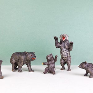 May include: Five brown and gray plastic bear figurines on a white surface with a light green background. The bears are in various poses, including standing, sitting, and lying down.