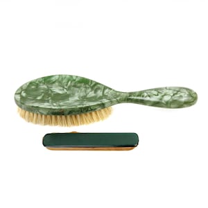 May include: A green and white marbled oval-shaped hair brush with a wooden handle. The brush has natural bristles and is shown next to a green rectangular box.