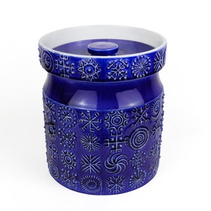 May include: A blue ceramic jar with a white lid, decorated with a pattern of white snowflakes and geometric shapes.