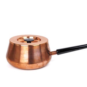 May include: A copper-colored saucepan with a black handle and a matching lid. The pot has a rounded base and a cylindrical body. The handle is angled and attached to the side of the pot.
