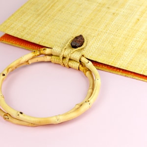 Puede incluir: Un bolso tejido de color marr&oacute;n claro con un asa de bamb&uacute; natural. El bolso tiene un forro de color naranja claro.