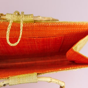 Puede incluir: Una bolsa de mano tejida de color beige y naranja con asas de bamb&uacute;. La bolsa est&aacute; abierta y se ve el interior. El interior de la bolsa est&aacute; forrado con tela naranja.