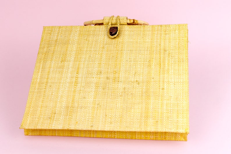 Puede incluir: Un bolso tote tejido de color beige claro con un asa de madera marr&oacute;n y un cierre de bot&oacute;n marr&oacute;n.