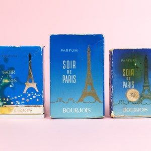Puede incluir: Tres cajas de perfume azules y doradas con el texto "Soir de Paris" y la Torre Eiffel en la parte delantera. Las cajas son de la marca Bourjois.