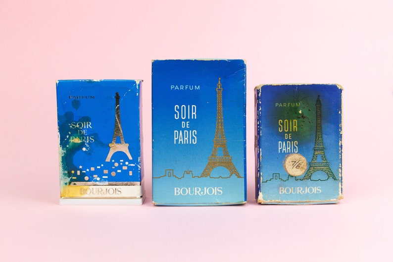 Puede incluir: Tres cajas de perfume azules y doradas con el texto "Soir de Paris" y la Torre Eiffel en la parte delantera. Las cajas son de la marca Bourjois.