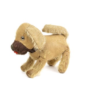 May include: A vintage plush toy dog with brown fur, a black nose, and a red mouth. The dog is standing on all four legs and has a fluffy tail.