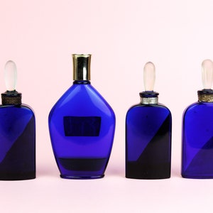May include: Four blue glass bottles with gold and silver accents. The bottles have different shapes and sizes. The bottles are arranged in a row on a pink background.