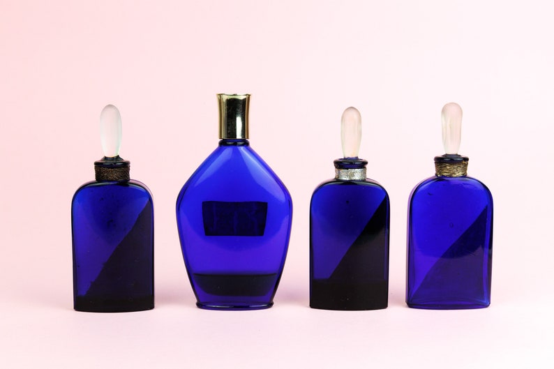 May include: Four blue glass bottles with gold and silver accents. The bottles have different shapes and sizes. The bottles are arranged in a row on a pink background.