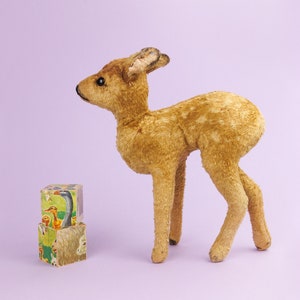 May include: A brown and tan plush toy deer with a long neck and long legs. The deer is standing on a purple surface next to a stack of colorful wooden blocks with animal illustrations.