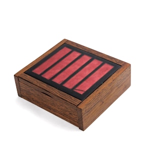 May include: A square wooden box with a dark brown wood grain finish. The lid features a black frame surrounding four parallel rectangular panels of deep red material, creating a geometric pattern on the top surface of the container.