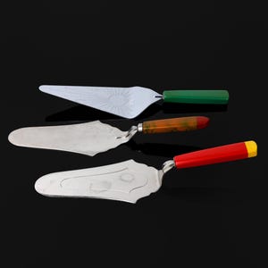 May include: Three silver cake servers with different colored handles. The top server has a green handle, the middle server has an orange handle, and the bottom server has a red and yellow handle.