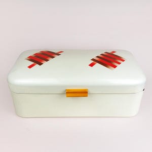 May include: White metal bread bin with a gold latch and red and brown geometric designs on the lid.