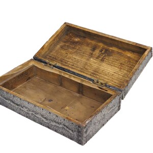 May include: An open wooden box with a hinged lid. The box is rectangular with a light brown interior and a textured, gray exterior. The lid is slightly ajar, revealing the inside of the box.