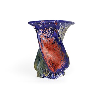 May include: A blue and red ceramic vase with a twisted, abstract design. The vase has a wide opening and a narrow base.