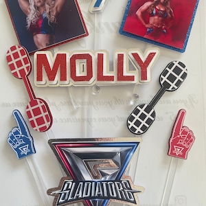 Puede incluir: Un conjunto de adornos para pasteles con una luchadora, el n&uacute;mero 7, la palabra "MOLLY", un logotipo de gladiador y dedos de espuma. La luchadora lleva un atuendo rojo, blanco y azul. El n&uacute;mero 7 es azul. La palabra "MOLLY" es roja. El logotipo del gladiador es plateado, azul y rojo. Los dedos de espuma son rojos y azules.