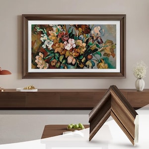 Puede incluir: Una pintura floral enmarcada con un marco de madera marrón oscuro. La obra de arte presenta un ramo de flores en tonos rosa, amarillo, blanco y verde. Se muestra una muestra del marco en primer plano.