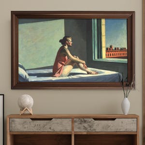 Pode incluir: Uma impressão emoldurada de uma pintura que retrata uma mulher em um vestido vermelho sentada em uma cama, olhando por uma janela. A pintura tem uma moldura marrom e está montada em uma parede bege. A cena inclui um edifício.