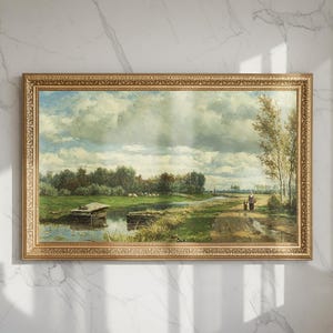 May include: A framed landscape painting with a gold ornate frame. The artwork depicts a serene river scene with a cloudy sky, lush green trees, and a path where a person is walking. The painting has a vintage aesthetic.