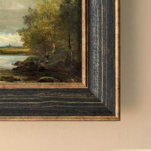 Könnte beinhalten: Gerahmtes Landschaftsgemälde mit einer Flusslandschaft mit Bäumen und einer angelnden Person. Der Rahmen ist in verwittertem Schwarz mit goldenen Akzenten gehalten, was dem Kunstwerk einen rustikalen Touch verleiht. Das Gemälde zeigt eine natürliche Umgebung.