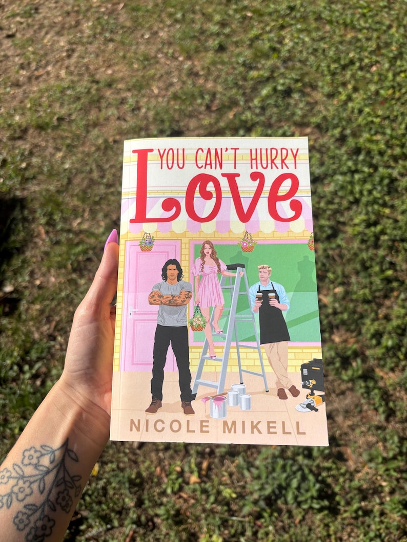 Pu&ograve; includere: Un libro tascabile intitolato "YOU CAN'T HURRY LOVE" di Nicole Mikell. La copertina presenta illustrazioni di tre persone, un edificio rosa e una scala. Il titolo &egrave; in grandi lettere rosse.