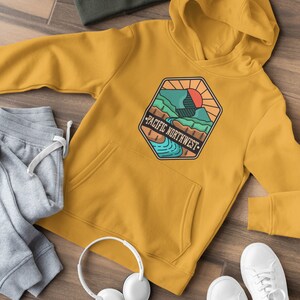 May include: A mustard yellow hoodie with a graphic of a mountain range and a river with the text "Pacific Northwest" in a vintage style.
