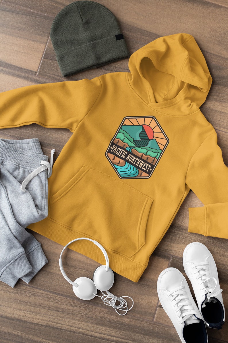 May include: A mustard yellow hoodie with a graphic of a mountain range and a river with the text "Pacific Northwest" in a vintage style.