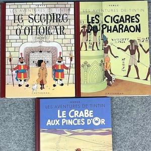 May include: Three vintage comic books featuring The Adventures of Tintin. The covers are red with white text and illustrations. The titles are "The Scepter of Ottokar", "The Cigars of the Pharaoh", and "The Crab with the Golden Claws".