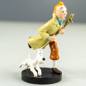 Könnte beinhalten: Eine Figur eines Comic-Charakters mit roten Haaren, der einen gelben Mantel und eine braune Hose trägt und einen Schraubenschlüssel hält. Der Charakter rennt mit einem weißen Hund an seiner Seite.