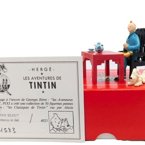 May include: A red box with a white label that reads "LES AVENTURES DE TINTIN" and "N° 1583". The box contains a figurine of Tintin sitting at a table with a dog. The figurine is made of white painted metal. The box also includes a certificate of origin.