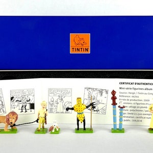 Könnte beinhalten: Eine blaue Box mit einem Echtheitszertifikat für einen Satz von sechs Miniaturfiguren aus der Tintin-Comicserie. Die Figuren basieren auf den Charakteren aus dem Album Tintin im Kongo. Das Zertifikat trägt den Titel "Certificat d'Authenticité Tintin" und enthält Details zu den Figuren, darunter die Quelle, die Referenznummer, das Produktionsjahr und die limitierte Auflagennummer.