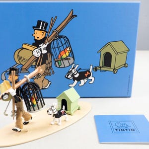 Könnte beinhalten: Ein Figurenset mit Tintin und Kapitän Haddock aus der Comic-Serie Die Abenteuer von Tintin. Das Set enthält eine blaue Box mit einer bunten Illustration der Figuren, eine Holzbasis und zwei Figuren. Die Figuren sind aus Metall und in leuchtenden Farben bemalt. Das Set ist ein tolles Geschenk für Fans der Comic-Serie.