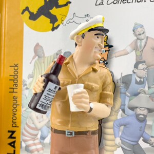 May include: A figurine of a cartoon character wearing a captain's hat and holding a bottle of alcohol and a cup. The character is wearing a brown shirt and pants. The figurine is part of a collection of cartoon characters.