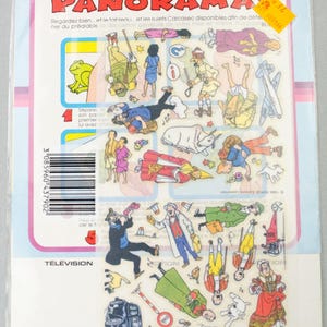Puede incluir: Una l&aacute;mina de pegatinas de dibujos animados vintage en una funda de pl&aacute;stico. Las pegatinas presentan varios personajes y objetos, incluyendo un coche rojo, una rana y una persona con un vestido rojo. El texto "ANIMEZ CE GRAND PANORAMA" est&aacute; en la parte superior.