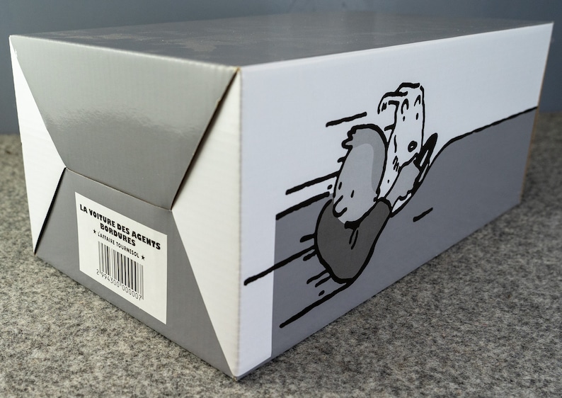 Puede incluir: Una caja de cart&oacute;n gris y blanca con una ilustraci&oacute;n de dibujos animados de un personaje en un coche. La caja tiene el texto "LA VOITURE DES AGENTS BORDURES" y un c&oacute;digo de barras.
