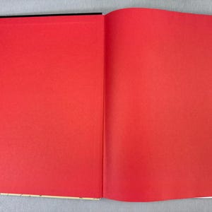 Puede incluir: Un libro abierto con p&aacute;ginas de color rojo brillante. La p&aacute;gina izquierda es totalmente visible, mientras que la p&aacute;gina derecha es parcialmente visible. El lomo del libro es negro y los bordes de las p&aacute;ginas son blancos.