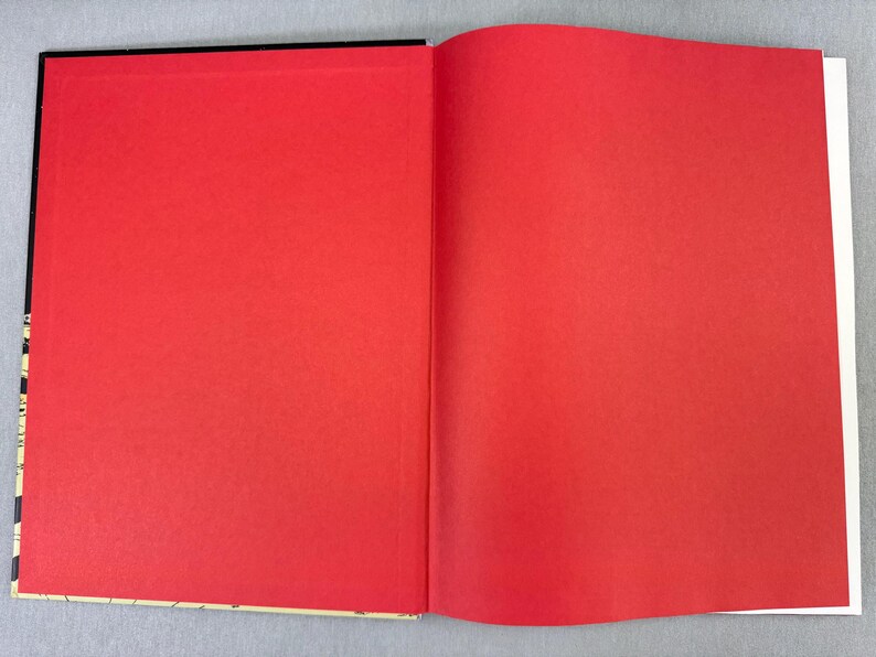 Puede incluir: Un libro abierto con p&aacute;ginas de color rojo brillante. La p&aacute;gina izquierda es totalmente visible, mientras que la p&aacute;gina derecha es parcialmente visible. El lomo del libro es negro y los bordes de las p&aacute;ginas son blancos.