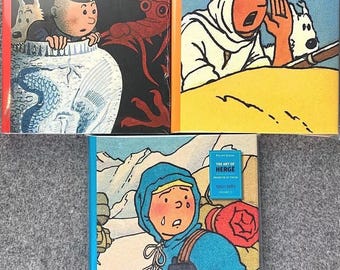 May include: Three hardcover books featuring illustrations from "The Art of Hergé" series. The covers display colorful comic art, with text labels indicating volume numbers and publication years. The books are in protective plastic.