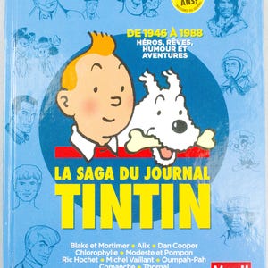 May include: A blue book cover featuring the character Tintin and his dog Snowy. The title "LA SAGA DU JOURNAL TINTIN" is in large yellow letters. The cover also includes the text "DE 1946 &Agrave; 1988" and "70 ANS!" with illustrations of other characters.