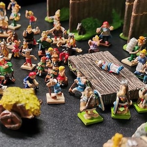 May include: A collection of colourful plastic figurines depicting characters from the Asterix comic series. The figurines are arranged on a wooden surface and include characters such as Asterix, Obelix, and Getafix.