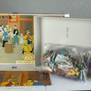 Peut inclure: Un puzzle de 100 pi&egrave;ces repr&eacute;sentant des personnages de la s&eacute;rie de bandes dessin&eacute;es Tintin. La bo&icirc;te du puzzle est ouverte, r&eacute;v&eacute;lant les pi&egrave;ces du puzzle dans un sac en plastique. La bo&icirc;te a une image de Tintin et de ses amis dans un march&eacute; chinois. La bo&icirc;te comprend &eacute;galement le texte "Puzzle 100" et "avec poster gratuit".
