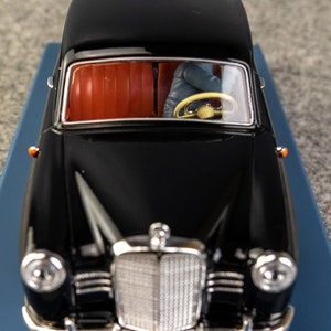 Puede incluir: Modelo de coche negro vintage con interior rojo. El coche tiene una parrilla cromada, faros y una placa de matr&iacute;cula que dice "8264F". El volante es amarillo. El modelo est&aacute; sobre una superficie azul.